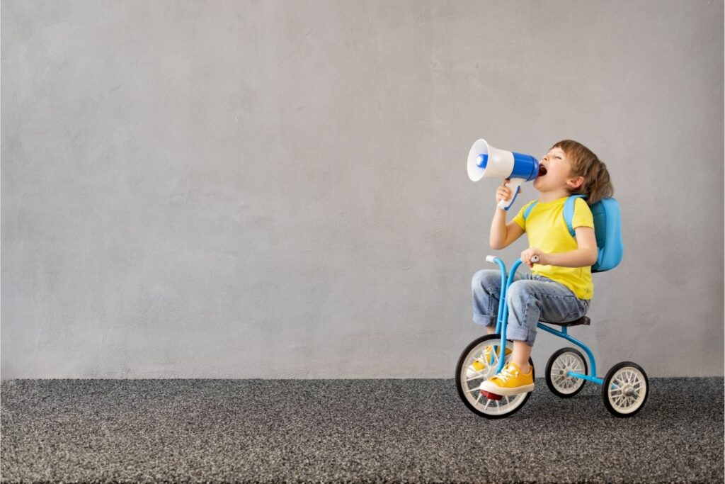 child riding a tricycle, while yelling into a plastic megaphone